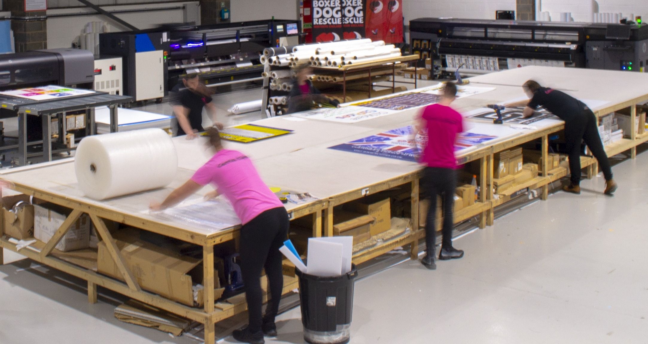 Workers in a warehouse producing and preparing signage for printing and installation.