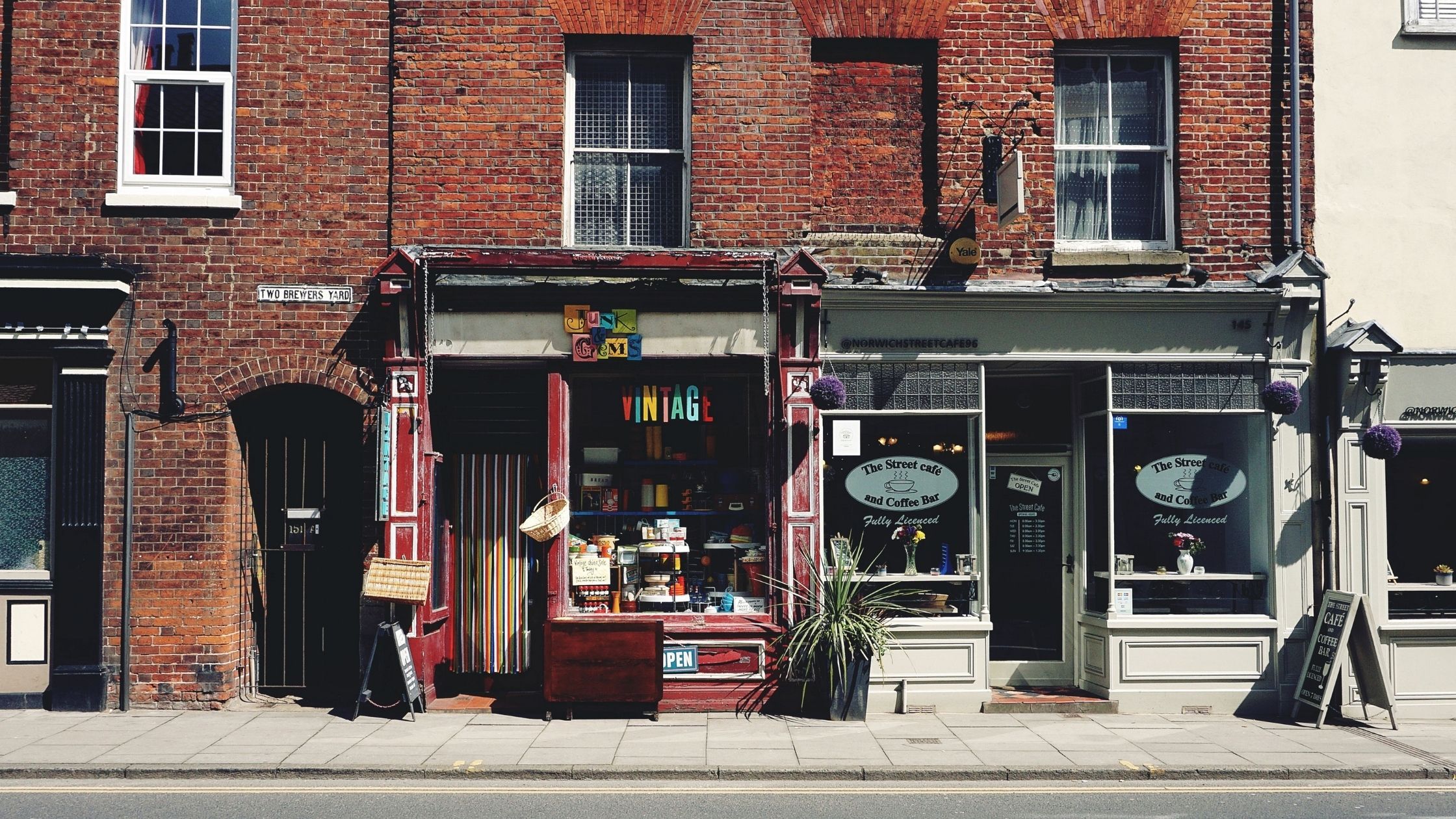 Two small independent shops on a busy high street, including a vintage clothing store and café, highlighting the importance of local business visibility.